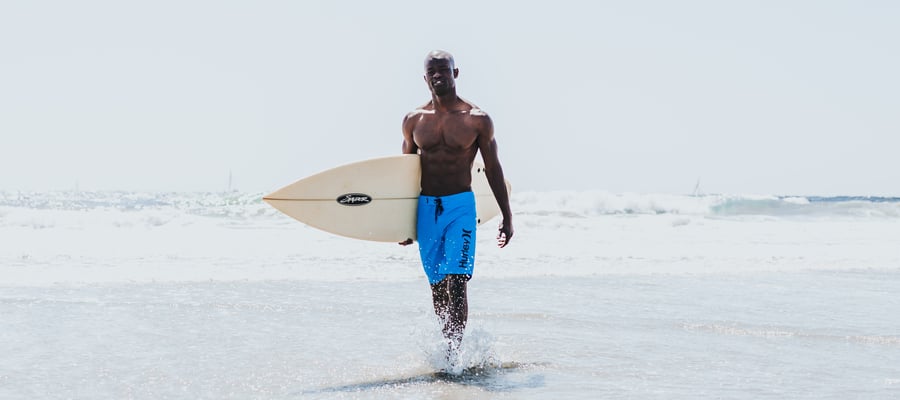 Man walking with surfboard in blue Hurley boardshorts
