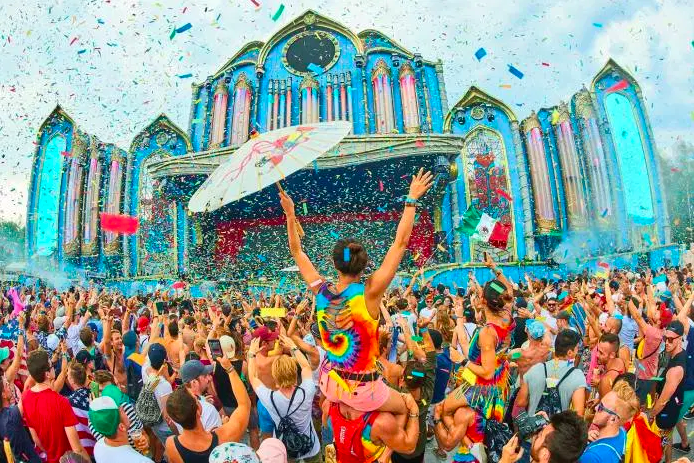 Tomorrowland festival attendees raise their hands amid confetti.