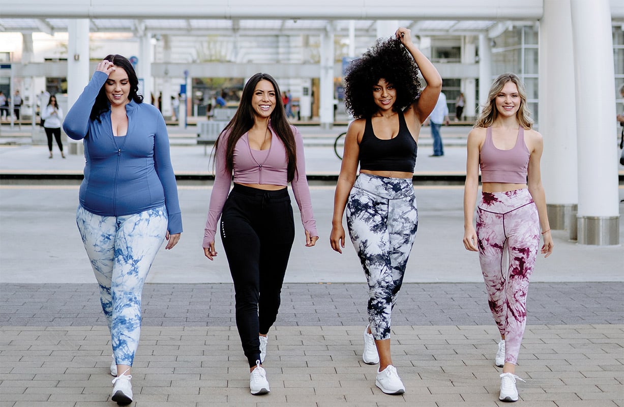 Four women model Balance Athletica athleisure sets in a public walkway. 