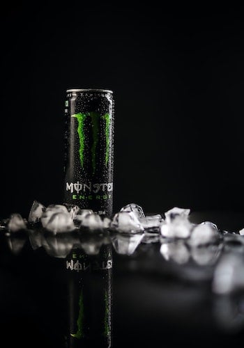 A can of Monster Energy drink surrounded by ice cubes against a black background, by Gkphotography 53. 