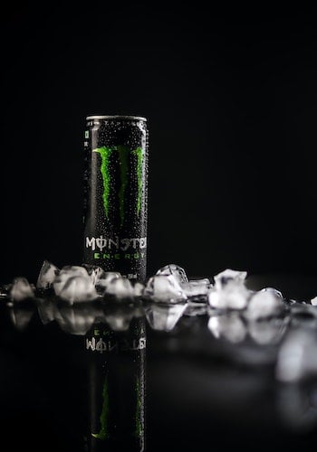A can of Monster Energy drink surrounded by ice cubes against a black background, by Gkphotography 53.