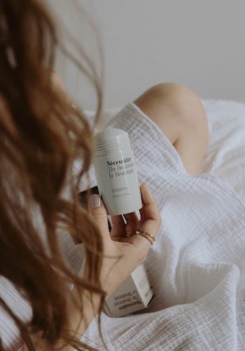A woman holding deodorant from clean beauty brand Nécessaire, by Mathilde Langevin. 