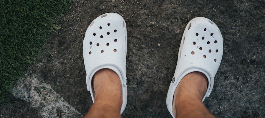 A pair of white Crocs sandals on a person’s feet, by Nathan Dumlao. 