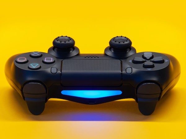 A close-up image of a video game controller against a bright yellow background, by Igor Karimov via Unsplash.