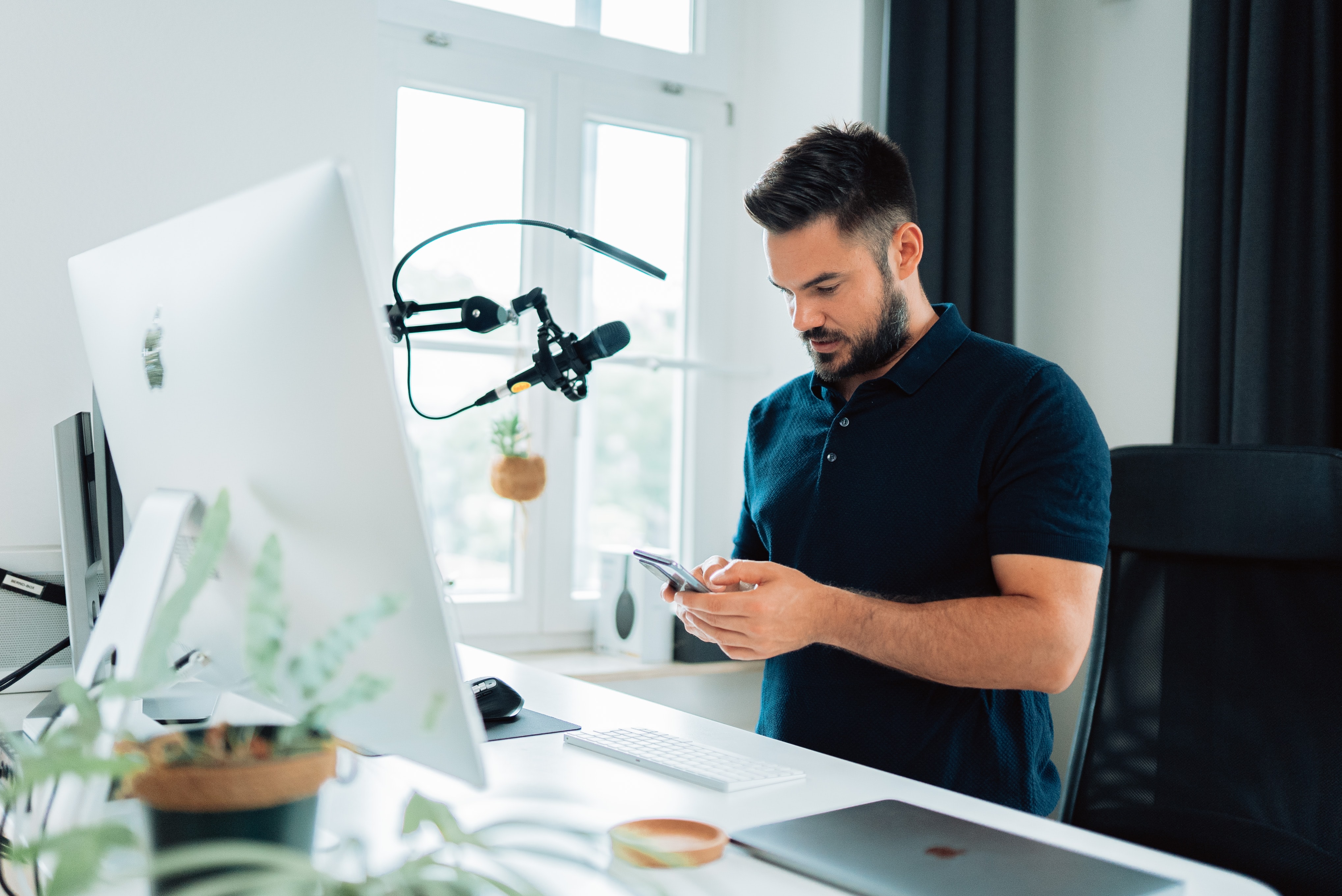 A man who has a monitor and mic equipment gazes at his phone.