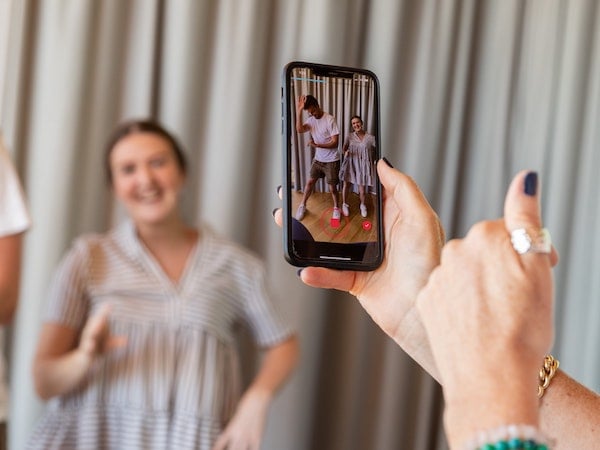 A woman performs a TikTok dance while being filmed on a smartphone, by S O C I A L . C U T via Unsplash.