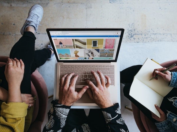 Three people seated in front of a laptop viewing social media content, by Windows via Unsplash.