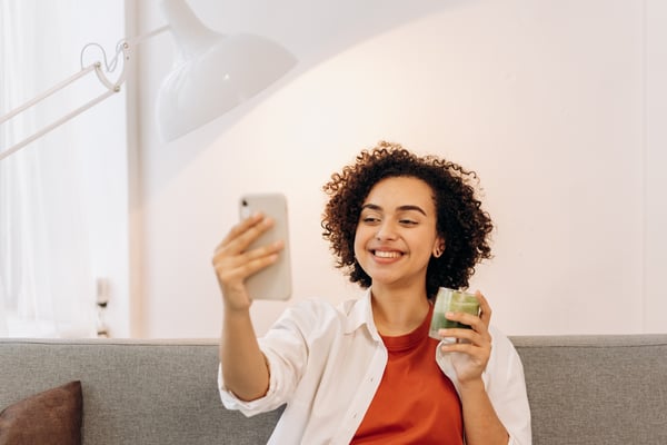 An influencer smiles at her phone while holding a green beverage