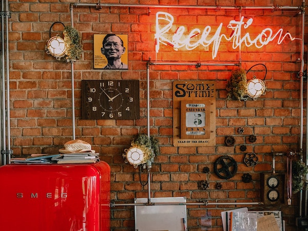 A red smeg fridge against an exposed brick wall with vintage posters and a clock, by Anastasiia Balandina via Unsplash.