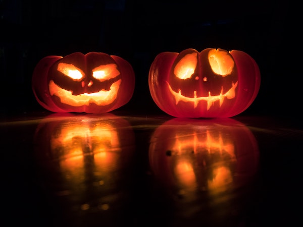Two Halloween jack-o-lanterns against a black background, by David Menidrey via Unsplash.