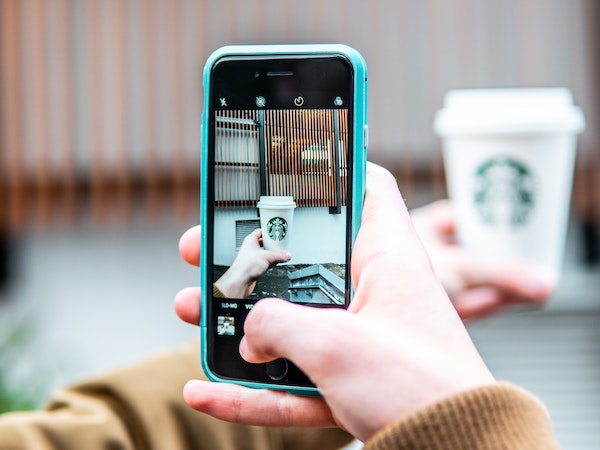 An influencer taking a photo of a Starbucks coffee with a smartphone, by Douglas Bagg via Unsplash.