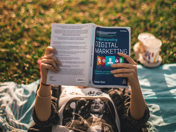 A person reading a tiktok affiliate marketing book in a field, by Elio Santos via Unsplash.