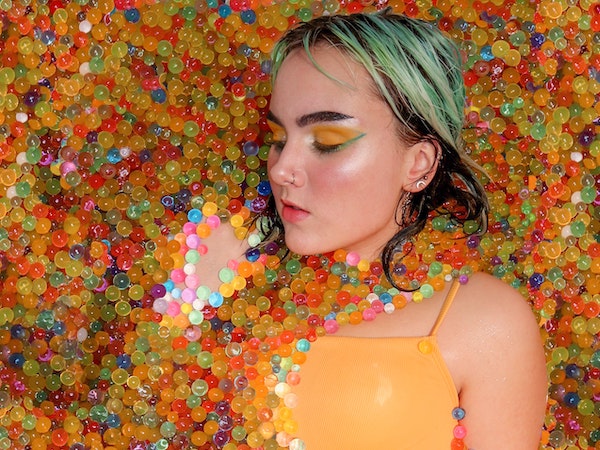 A TikTok creator wearing colorful eyeshadow immersed in rainbow beads, by Isi Parente via Unsplash.