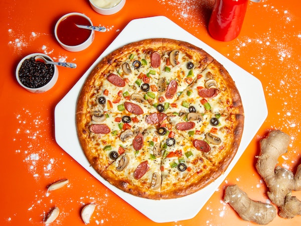 A DiGiorno pizza on an orange table with condiments, by Shourav Sheikh via Unsplash.